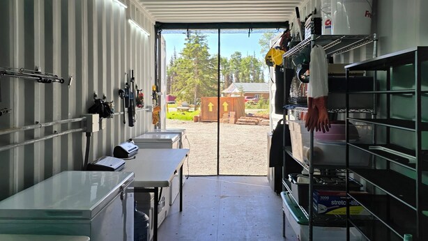 A kitchen with stainless steel appliances, a sink, and a window with a view of trees and a building outside. - Kenai River RV at Fish Camp + Processing (Soldotna)