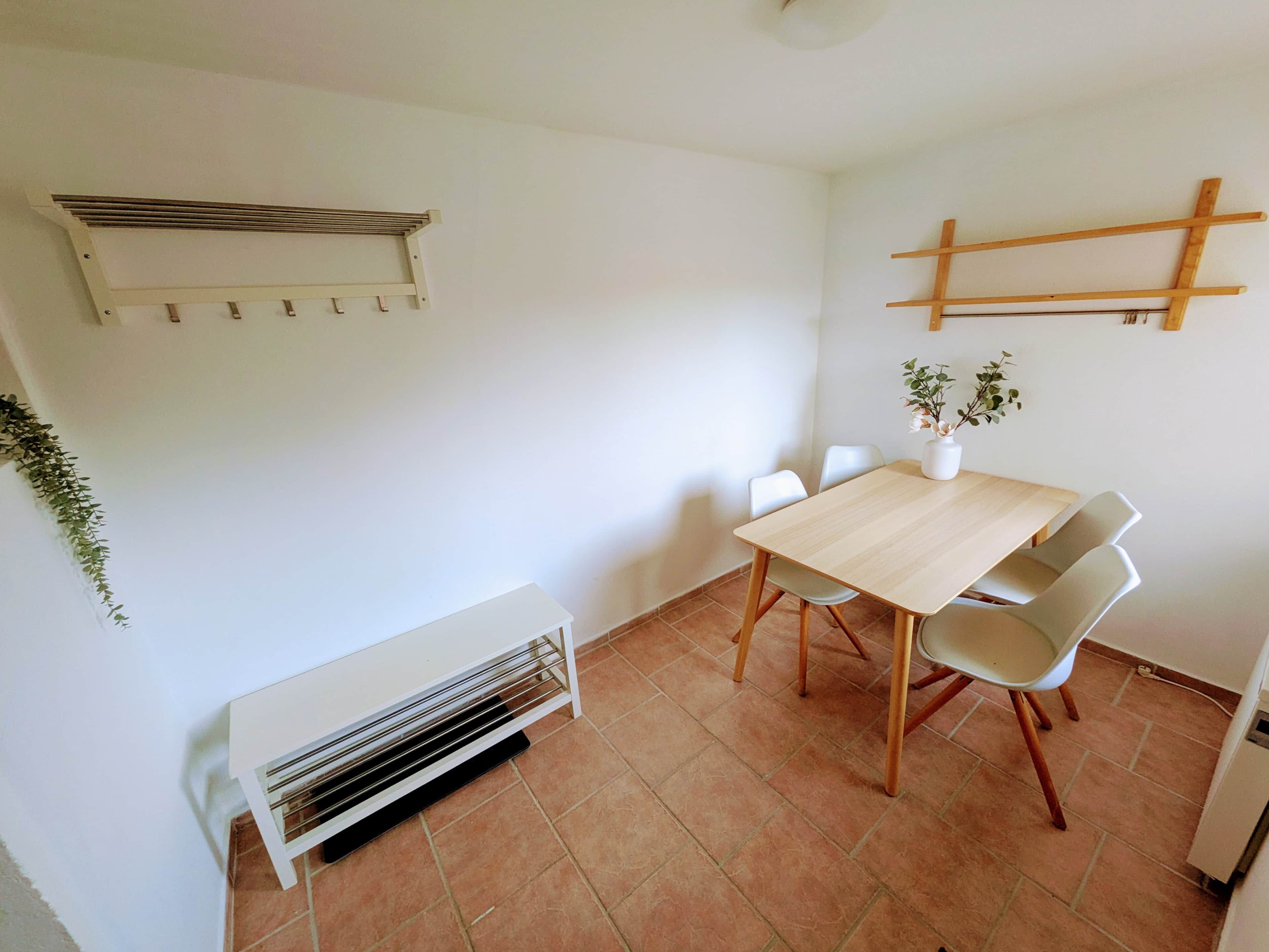 A dining area with a wooden table and chairs, a white radiator, and a plant on the wall.