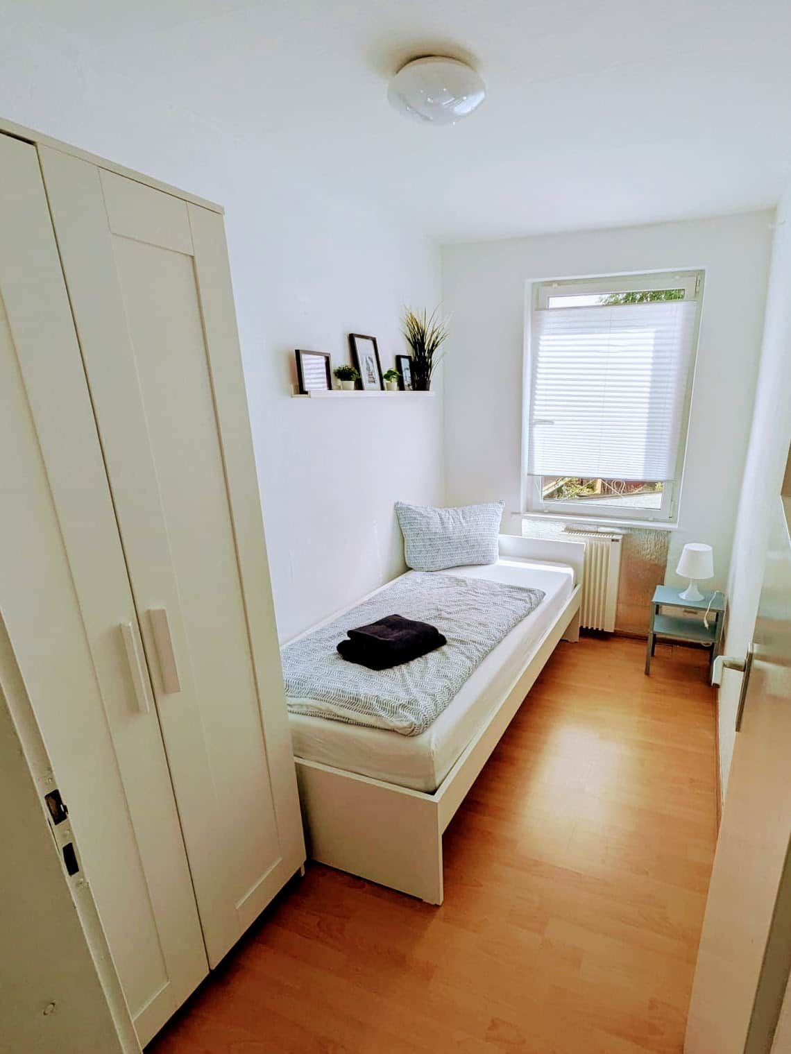 A compact bedroom with a bed, a small window, a radiator, and a wardrobe.