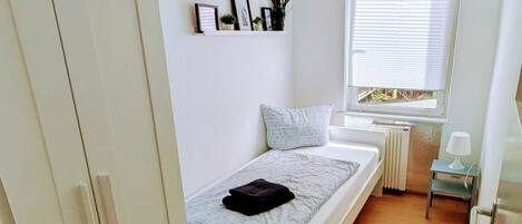 A compact bedroom with a bed, a small window, a radiator, and a wardrobe.