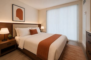 A hotel room with a large bed, two bedside tables with lamps, a framed picture on the wall, and a large window with blinds. - The Dominion Suites (Toronto)