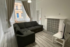 A living room with a sofa, a small table, a patterned wall, and a window with curtains. - Property (Glasgow)