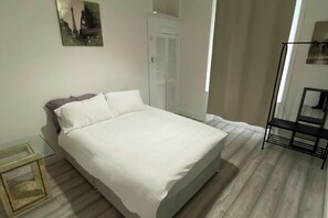 A bedroom with a bed, a bedside table, a chair, and a door. - Property (Glasgow)