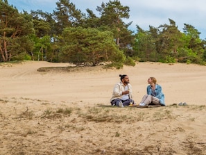 Zwei Personen sitzen am Strand, im Hintergrund Bäume.