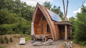 Een houten chalet met schuin dak, een klein terras, een vuurkuil en een bank.