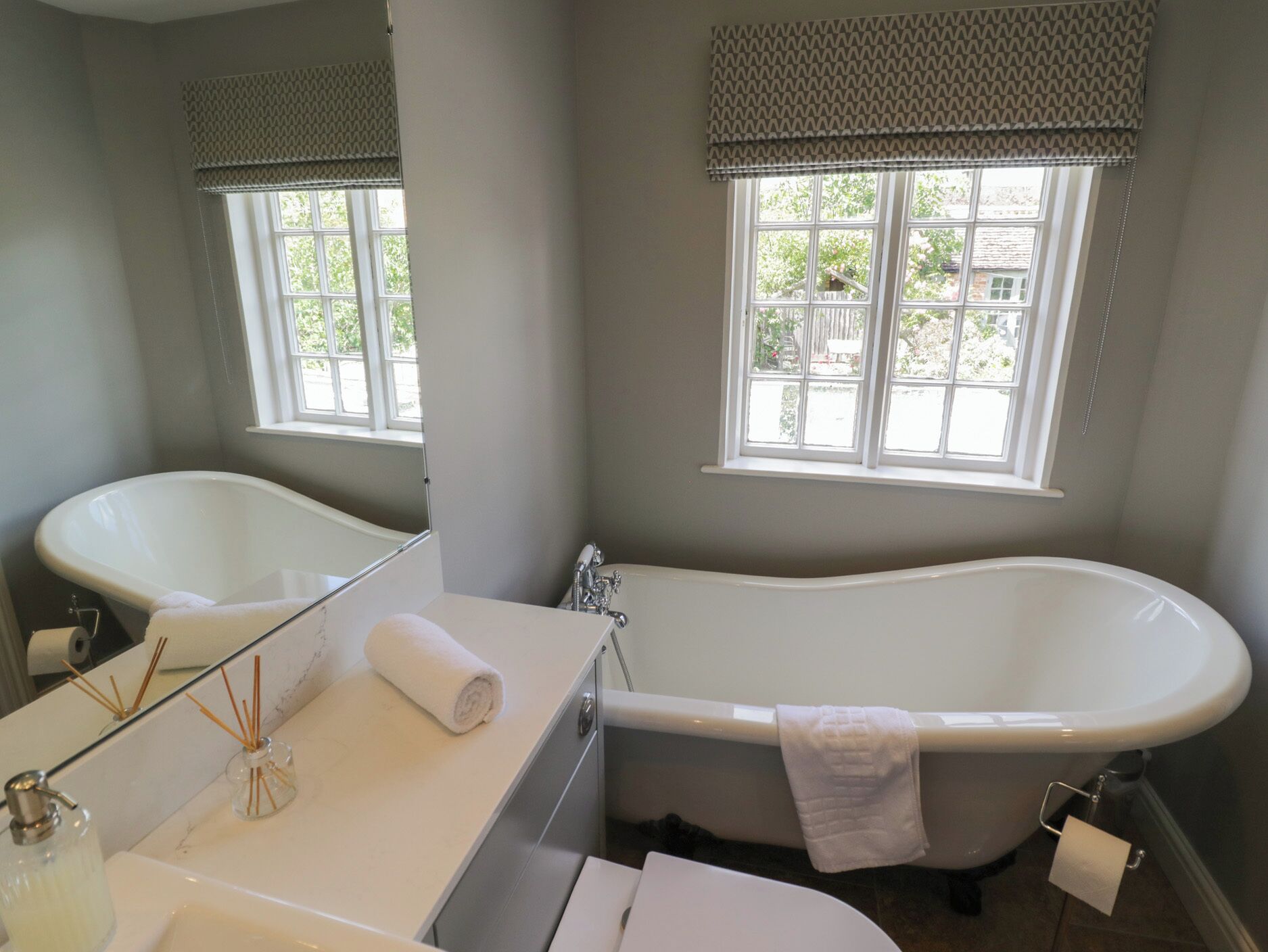A bathroom with a bathtub, a sink, a mirror, and a window with a view of the outside.