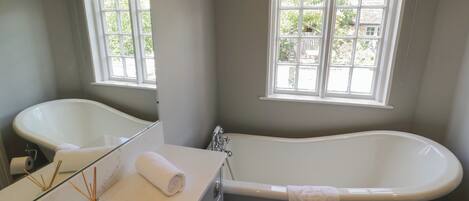 A bathroom with a bathtub, a sink, a mirror, and a window with a view of the outside.