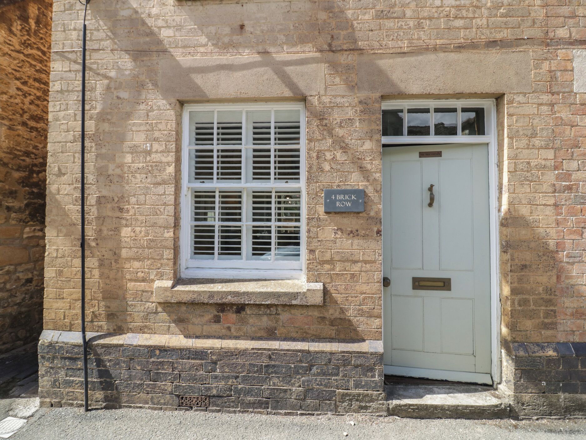 A brick building with a white door and window, a small ledge below the window, and a sign reading '4 BRICK ROW'.