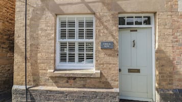 A brick building with a white door and window, a small ledge below the window, and a sign reading '4 BRICK ROW'.