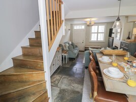 Una escalera conduce a un comedor con una mesa lista para dos personas, un sofá y una cocina al fondo.
