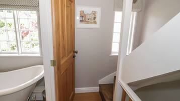 A narrow bathroom with a wooden door, a bathtub, and a window with blinds.
