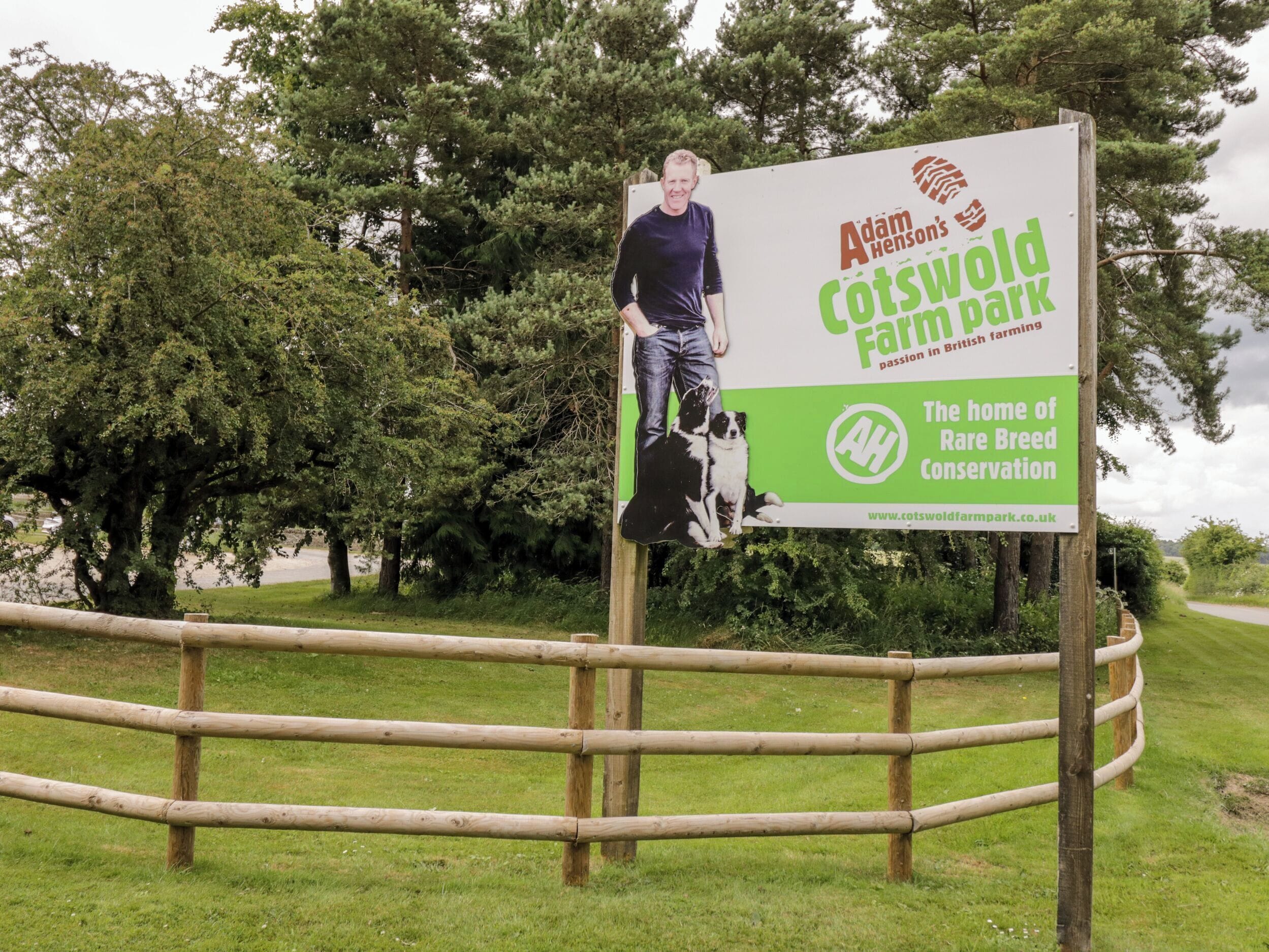 Un cartel para el Cotswold Farm Park de Adam Henson con una foto de un hombre y un perro.