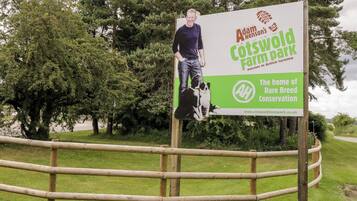 Un cartel para el Cotswold Farm Park de Adam Henson con una foto de un hombre y un perro.
