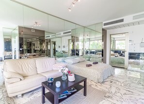 Ett modernt vardagsrum med en soffa, ett soffbord och en stor spegel som reflekterar rummet.