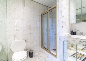 Un baño con inodoro, ducha envuelta en cristal, lavabo con espejo y azulejos de mármol.