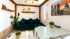 A living room with a green sofa, a glass table, a ceiling fan, and a cityscape painting.