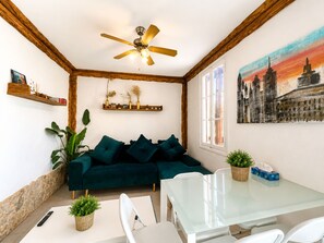 A living room with a green sofa, a glass table, a ceiling fan, and a cityscape painting.