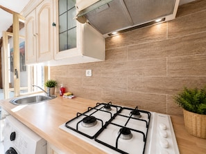 A modern kitchen with wooden cabinets, a gas stove, a sink, and a small plant. - Small House Downtown Near Monaco (Beausoleil)