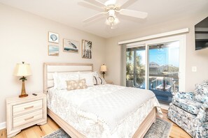 Ein Schlafzimmer mit einem Bett, Nachttischen, einem Deckenventilator, Kunstwerken an der Wand und Blick durch eine Schiebetür.