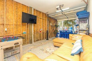 A room with a foosball table, a sofa, a television, and a bar area with stools. - Sunset Landing - 4 BR Home on Canal with Dock, Covered Porch, Pet Friendly! (Surf City)