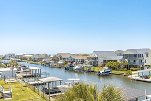 A marina with boats docked, a clear sky, and houses with balconies. - Sunset Landing - 4 BR home on Canal - covered porch, private dock, pet friendly! (Surf City)