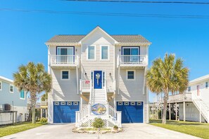 A two-story building with a central entrance, a blue door, and a sign that reads 'Sunset Landing.' - Sunset Landing - 4 BR Home on Canal with Dock, Covered Porch, Pet Friendly! (Surf City)