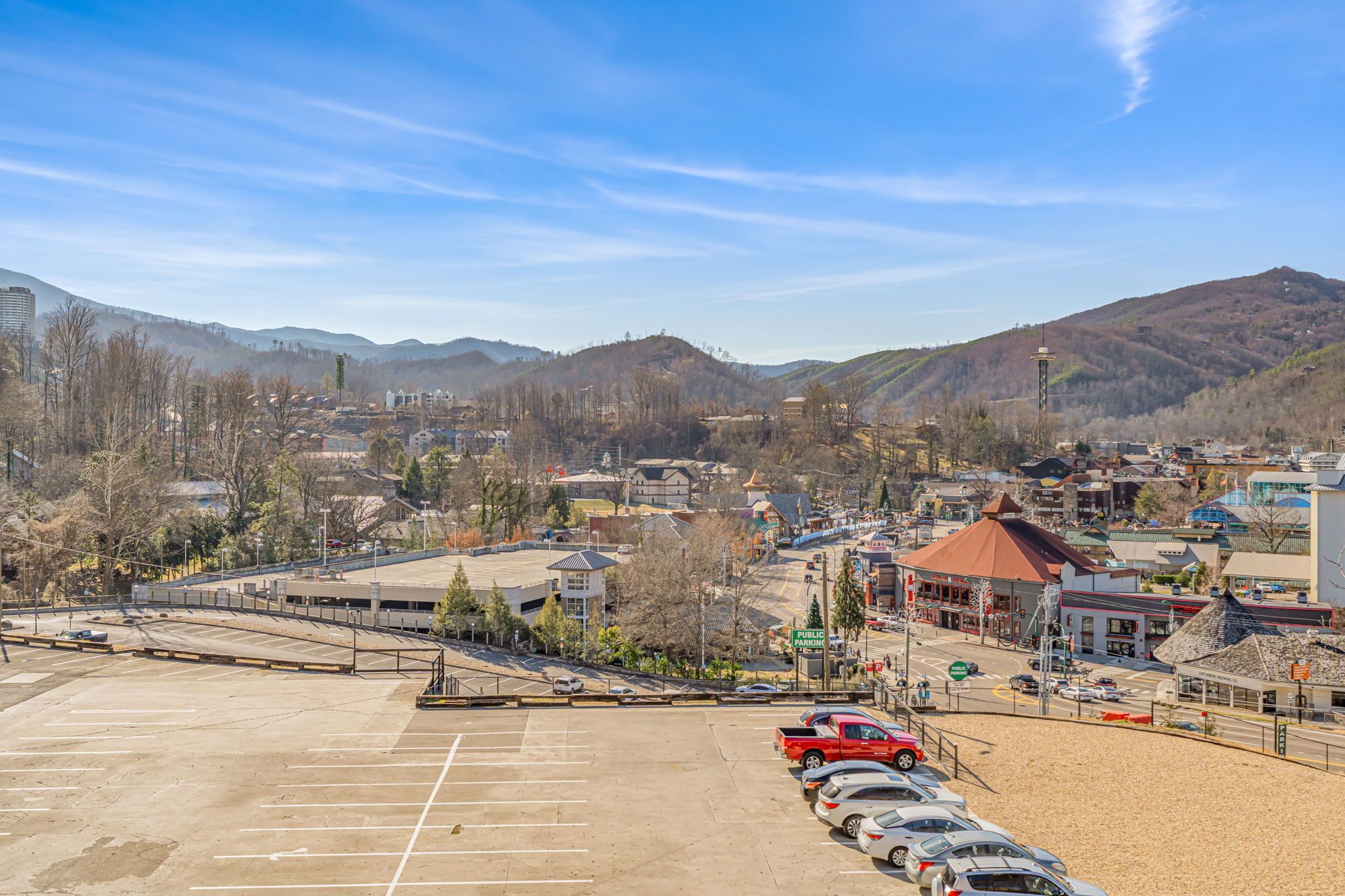 A parking lot with several cars, a public building, and a mountainous backdrop.