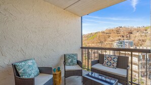 Ein Balkon mit Korbmöbeln, einem kleinen Tisch und Blick auf eine Hügelkuppe mit Gebäuden.