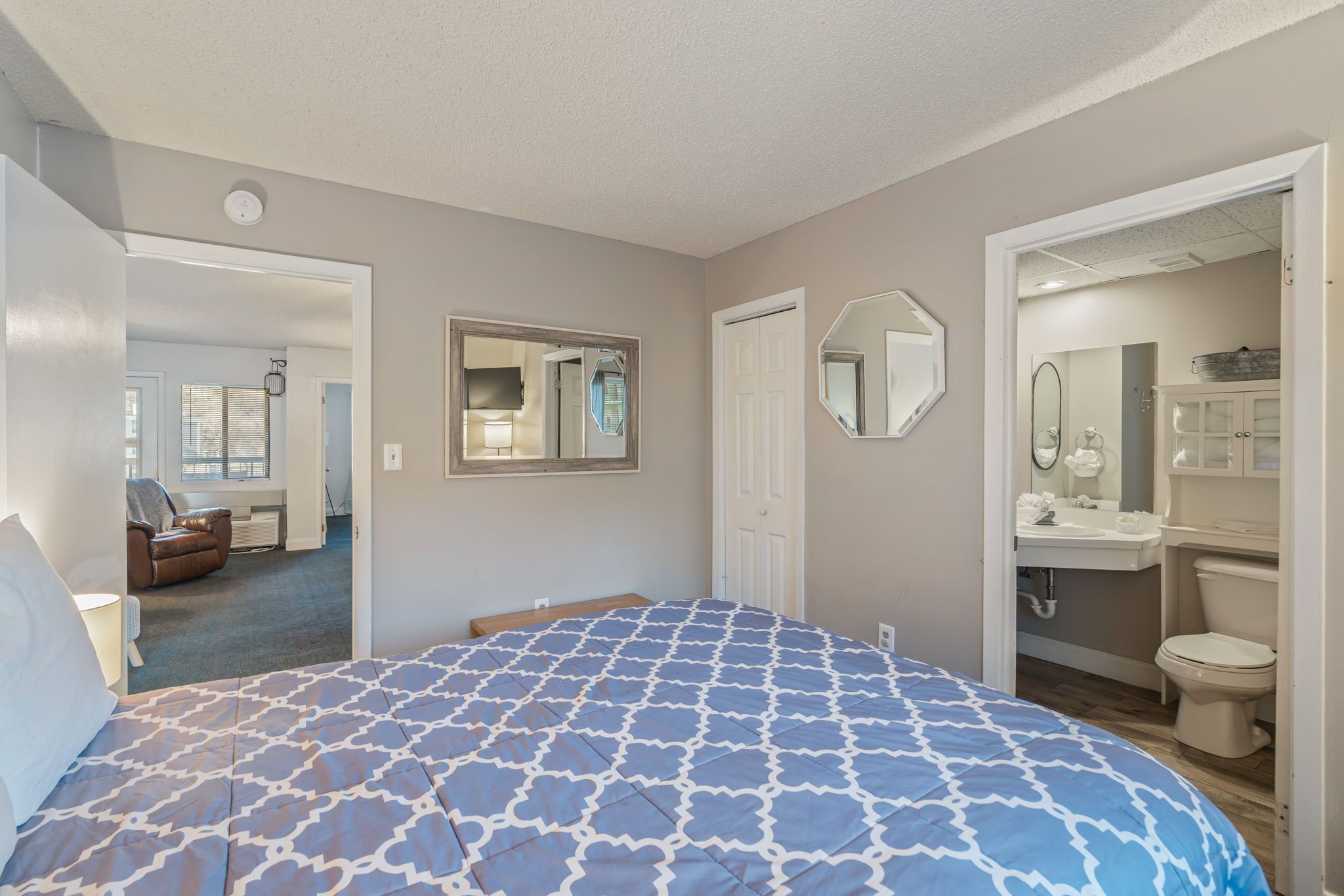 A bedroom with a large bed, a bathroom with a sink and toilet, and a hallway leading to another room.