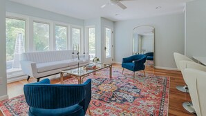 Uma sala de estar moderna com um sofá branco, cadeiras azuis, uma mesa de centro e uma janela grande.
