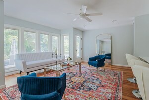 A modern living room with a white sofa, blue chairs, a coffee table, and a large window.