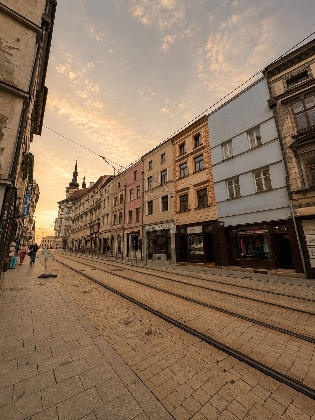 Une rue bordée de voies de tramway, des immeubles avec des boutiques et un ciel dégagé.