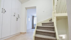 Un escalier menant à l’étage supérieur, un couloir avec une porte, et une armoire blanche à plusieurs portes.