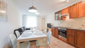 Une cuisine moderne avec des meubles en bois, une table à manger avec des chaises, un four encastré et un téléviseur.
