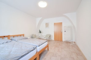 Una habitación con dos camas, una mesita con una planta, una silla y un armario.