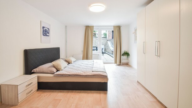 Une chambre  à coucher moderne, avec un lit, une table de chevet, une armoire et une vue sur l’extérieur.