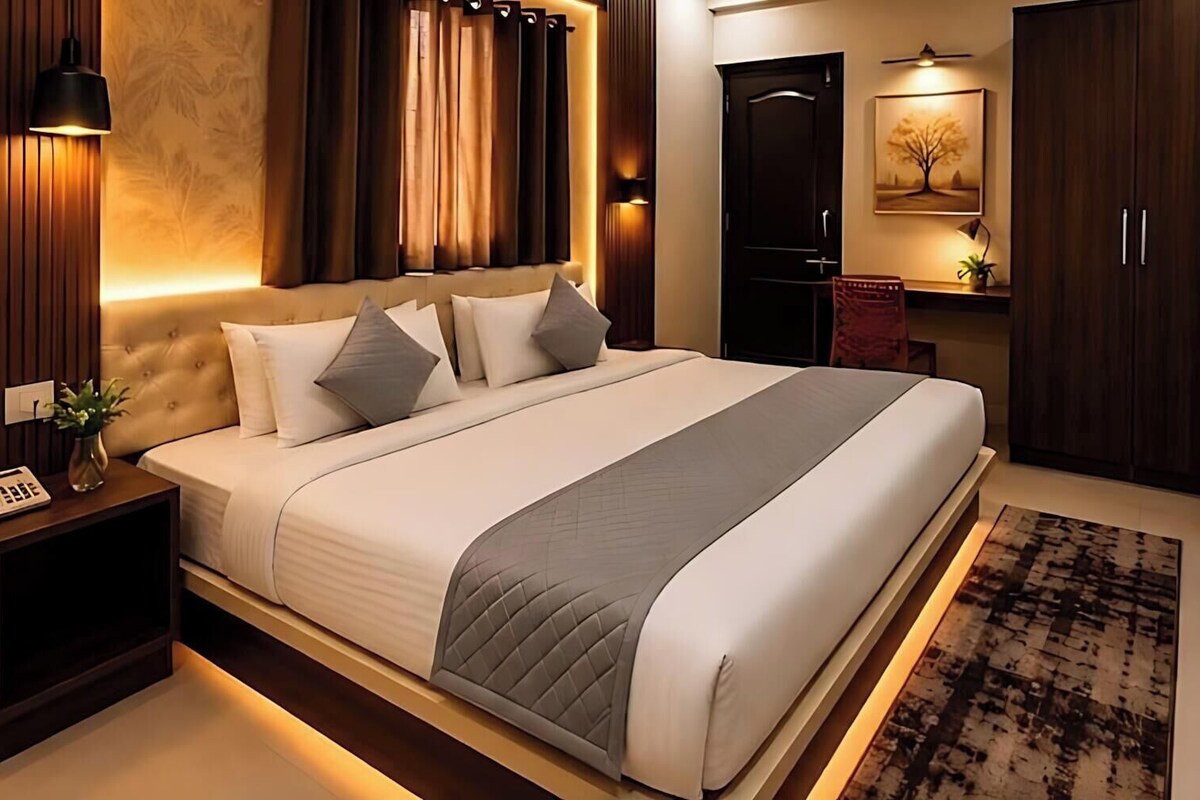A modern bedroom with a large bed, bedside lamps, a nightstand, a wardrobe, and a painting on the wall.