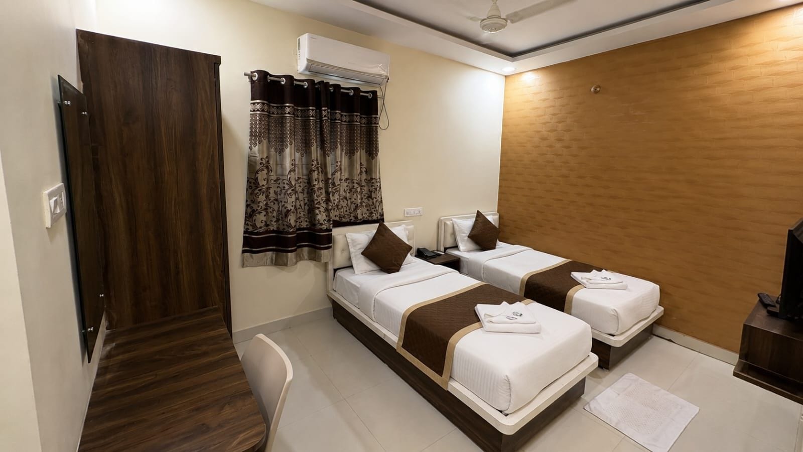 Een hotelkamer met twee bedden, een bureau, een stoel, een airconditioning en een televisie.