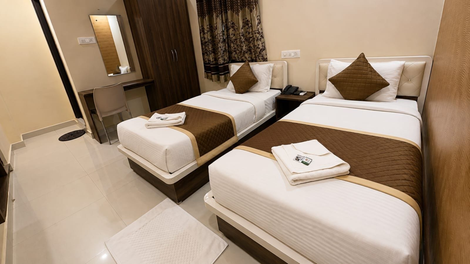 A hotel room with two beds, a desk, a mirror, and a wardrobe.