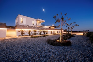 A modern two-story house with a balcony, a well-lit exterior, and a gravel driveway. - Villa AMore by Feel Croatia (Debeljak)