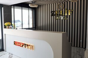 A reception desk with a sign that reads 'ZELIF HOTEL' and 'RECEPTION' illuminated.