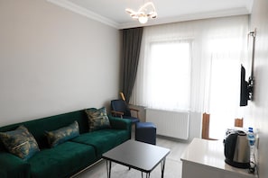 A modern living room with a green sofa, a small table, a chair, a radiator, and a television mounted on the wall.