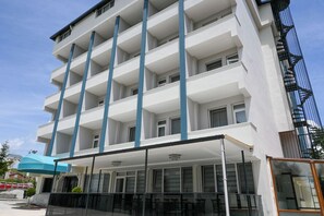 Un hotel de varios pisos con fachada plana, balcones y una zona de estar al aire libre cubierta.