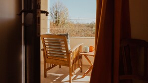 Una sedia e un tavolo di legno su un balcone con vista su alberi e cielo sereno.