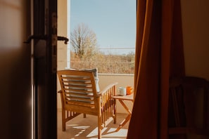 Et træbord og en træstol på en balkon med udsigt til træer og en blå himmel.