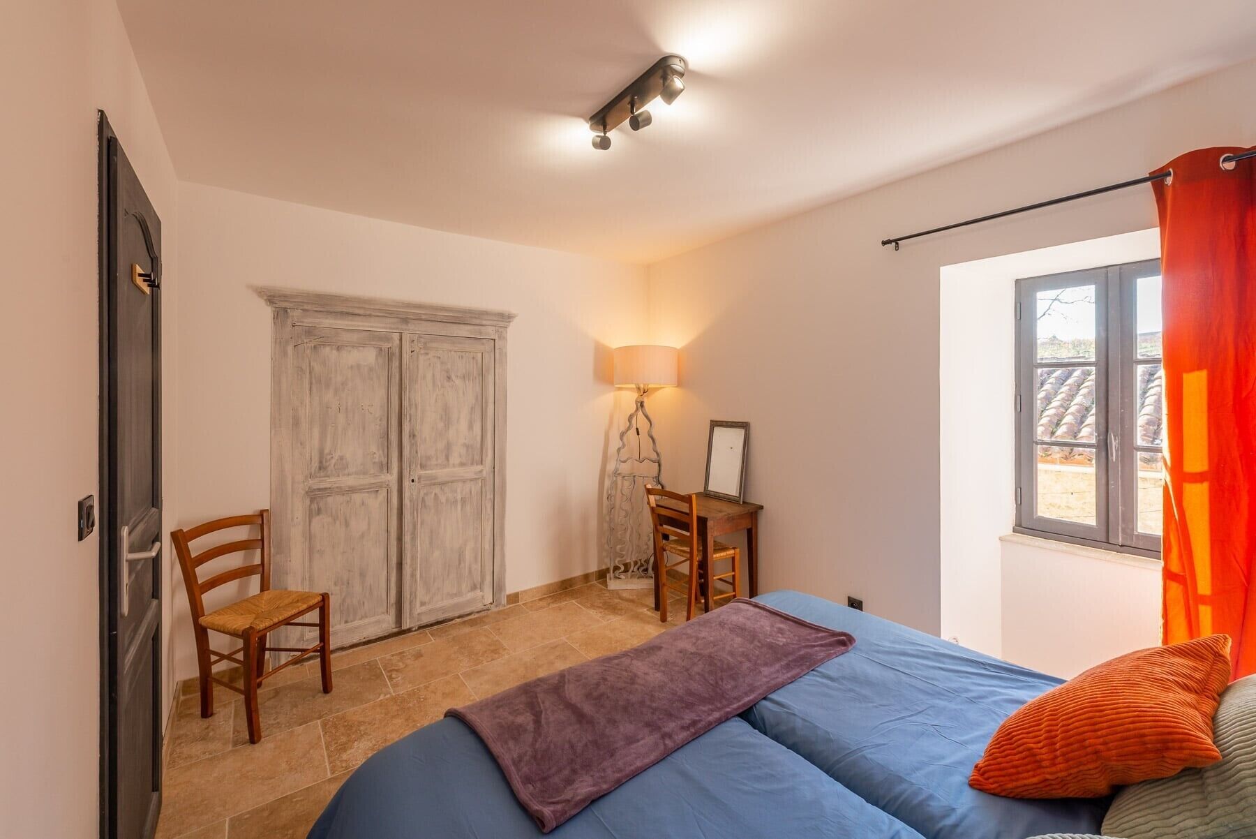 A bedroom with a bed, a desk, a chair, a wardrobe, and a window with curtains.