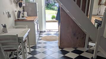 Een keuken met een geruite vloer, een eettafel, stoelen, een vloerkleed en een trap naar een andere kamer.