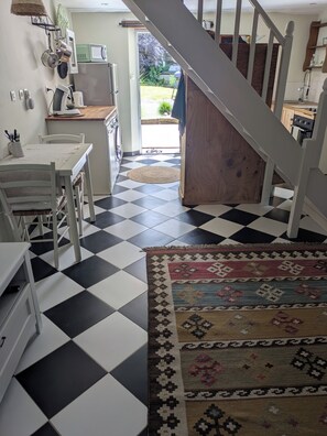 A kitchen with a checkered floor, a dining table, chairs, a rug, and a staircase leading to another room. - Small house in quiet village - Cosy cocoon cottage with garden (La Grée-Saint-Laurent)