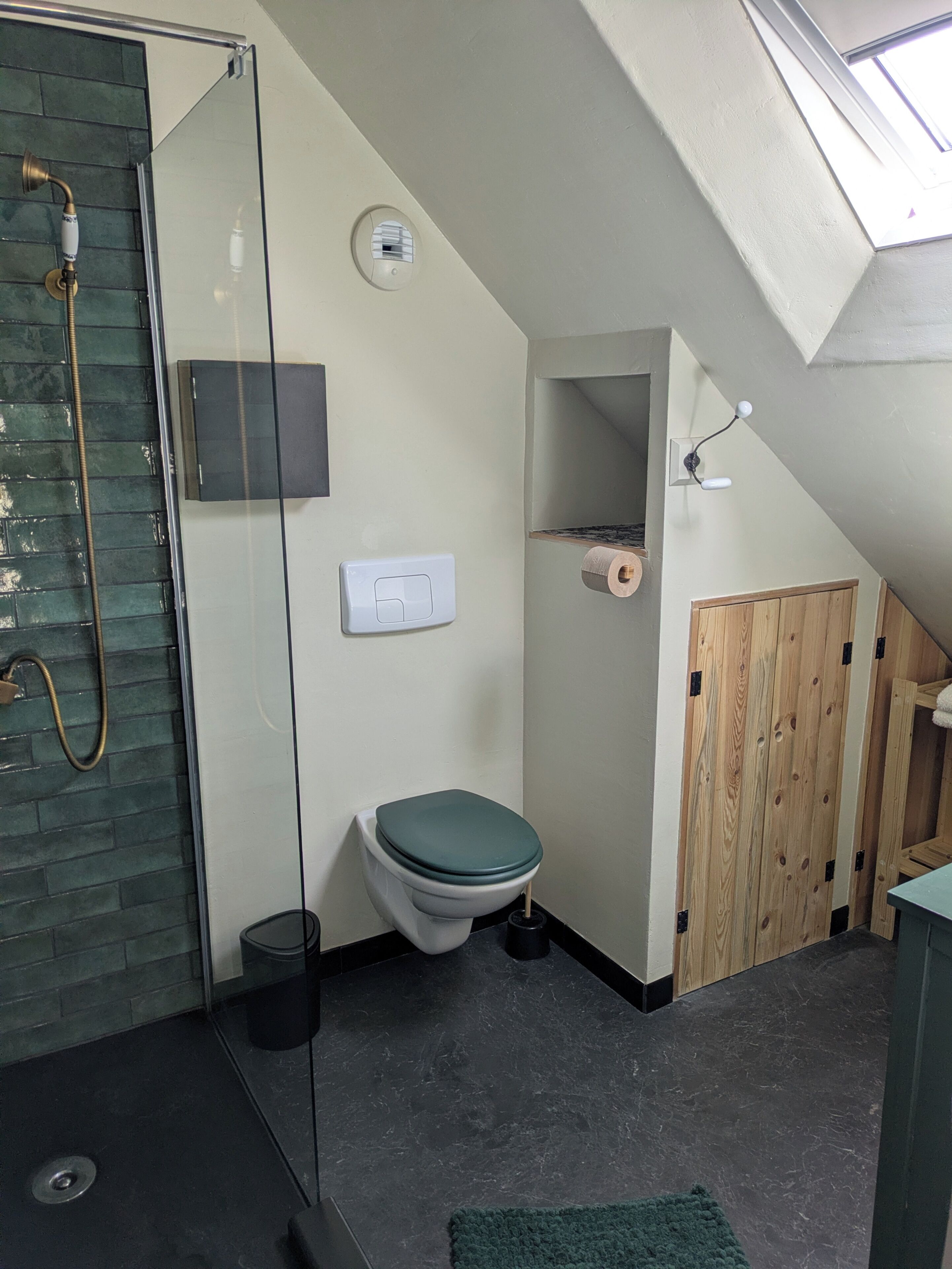 Een badkamer met een douchecabine van glas, een toilet, een bidet en een houten deur.