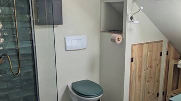 Een badkamer met een douchecabine van glas, een toilet, een bidet en een houten deur.